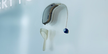 Behind-the-ear hearing aid with attached earpiece and cleaning tool on a light background
