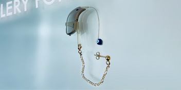 Modern hearing aid with transparent tubing, a blue earmold, and a retention clip displayed on a sleek surface.