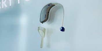 Behind-the-ear hearing aid with attached earpiece and cleaning tool on a light background