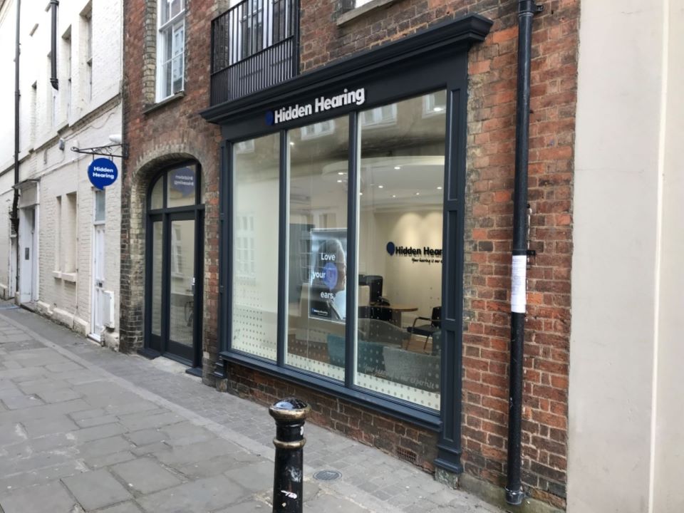 Hidden Hearing Bexleyheath clinic exterior on a brick-lined street with large windows displaying signage.