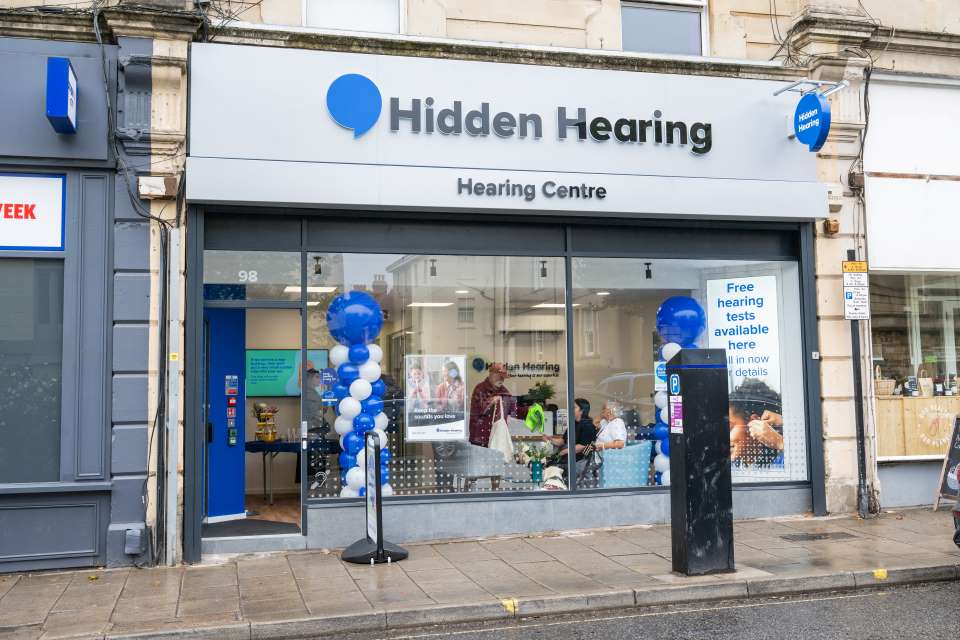 Exterior of Hidden Hearing clinic in Bristol, featuring a modern storefront with glass windows, a blue and white balloon display, and signage promoting free hearing tests.