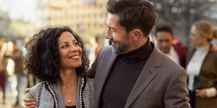 Man wearing a discreet hearing aid while walking outdoors with a companion in a lively urban setting
