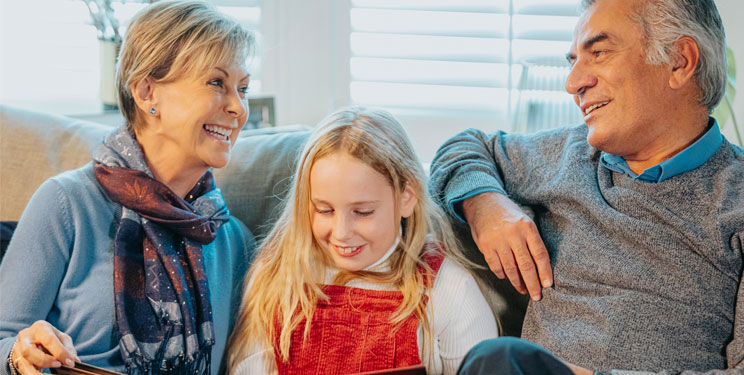 Grandparents bonding with their granddaughter while reading together on a cozy couch.