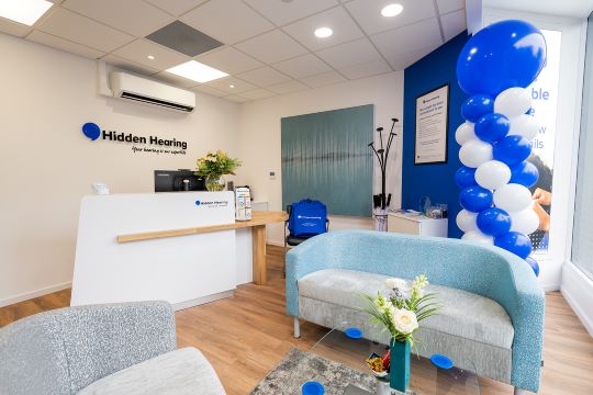 Reception area of the Hidden Hearing Bristol branch featuring a white counter, branded signage, and a cozy seating area.