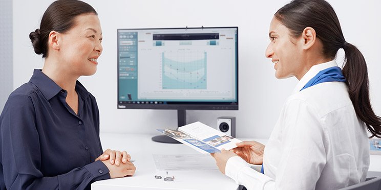 Hearing care professional discussing hearing aid options with a customer in a clinic setting.