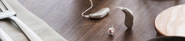 Oticon Opn hearing aid resting on a wooden dining table alongside cutlery and dishes.