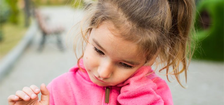 Young child wearing a pink sweater holding her ear with a pained expression, indicating possible ear discomfort or pain.