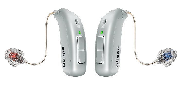Two silver Oticon hearing aids with slim tubing and dome earpieces (marked red for right, blue for left), featuring buttons and green LED indicators, designed for discreet, high-quality hearing care.
