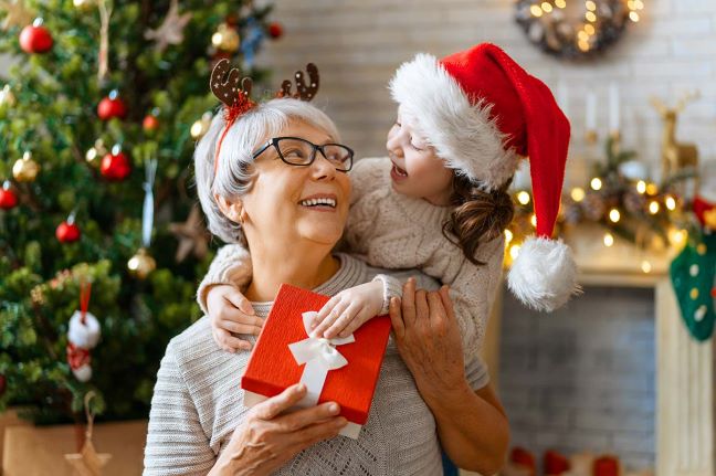 Festive holiday scene with a grandmother and child exchanging a gift near a decorated Christmas tree.