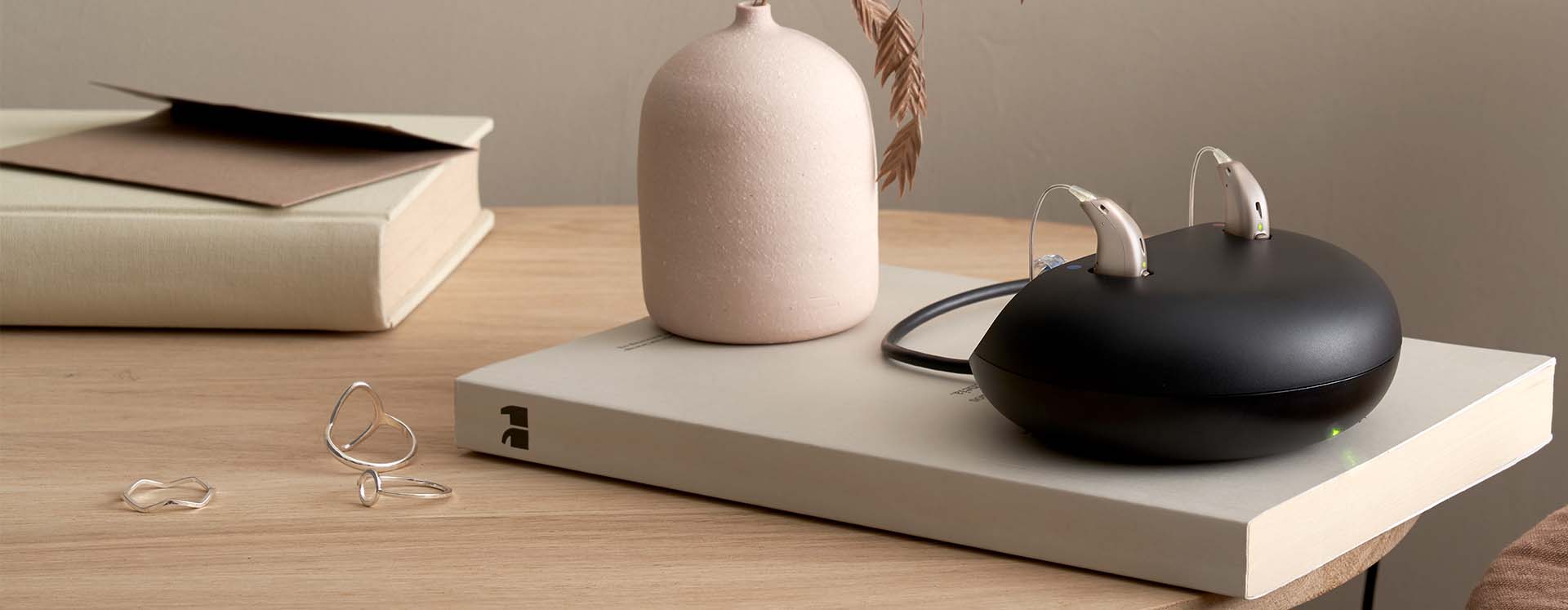 Rechargeable hearing aids in a sleek black charging case displayed on a wooden table alongside minimalist decor.