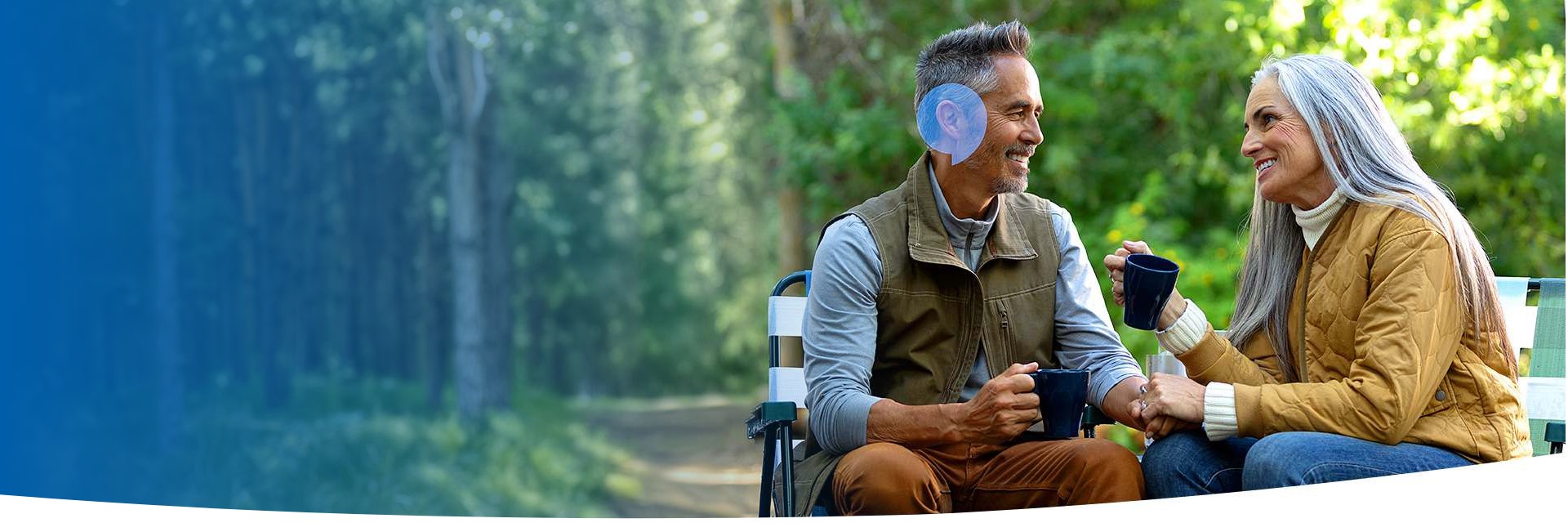 Elderly couple enjoying a conversation outdoors while holding coffee mugs.