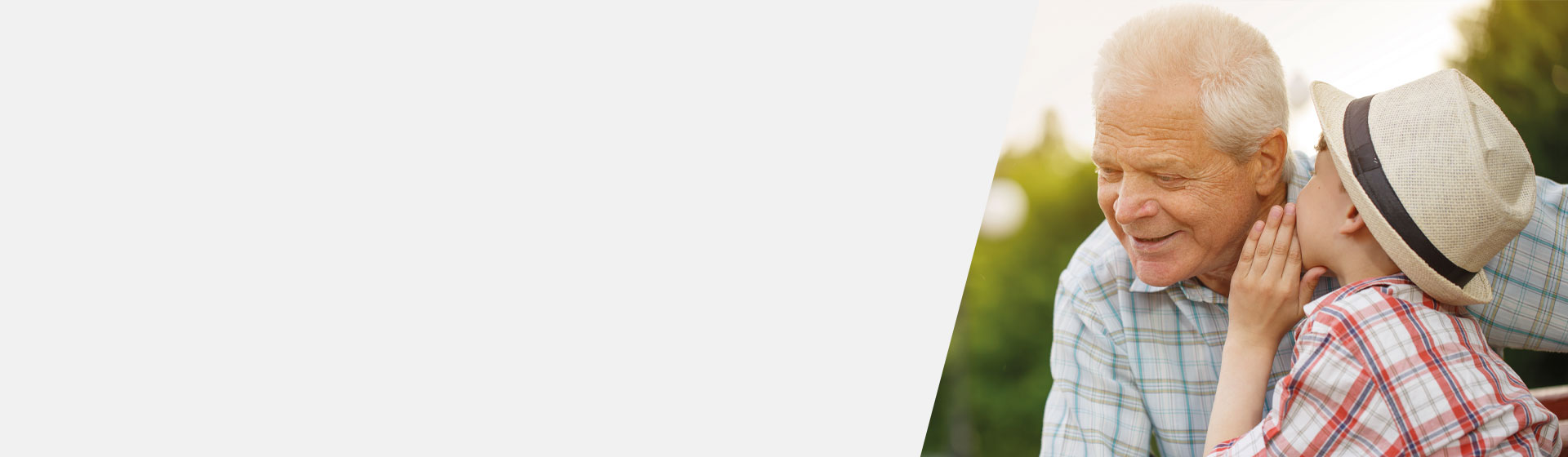 Grandchild wearing a straw hat whispering to his grandfather outdoors during a sunny day.