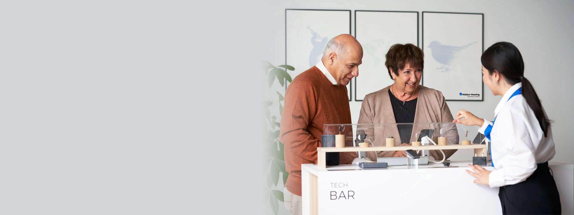 Hearing specialist explaining Bluetooth hearing aids to customers at a tech bar.