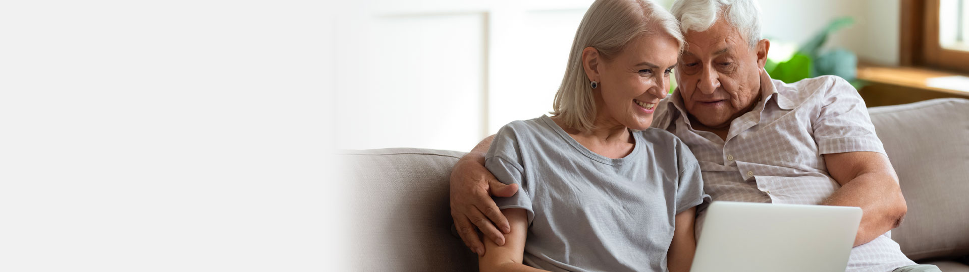 Elderly couple researching audiology services on a laptop while sitting on a couch.