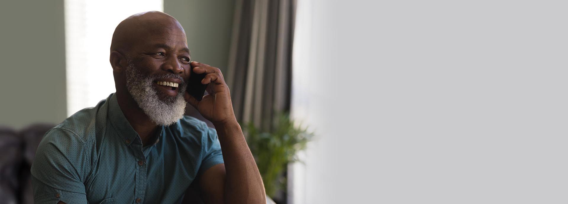 Man with a beard talking on the phone in a bright indoor setting.