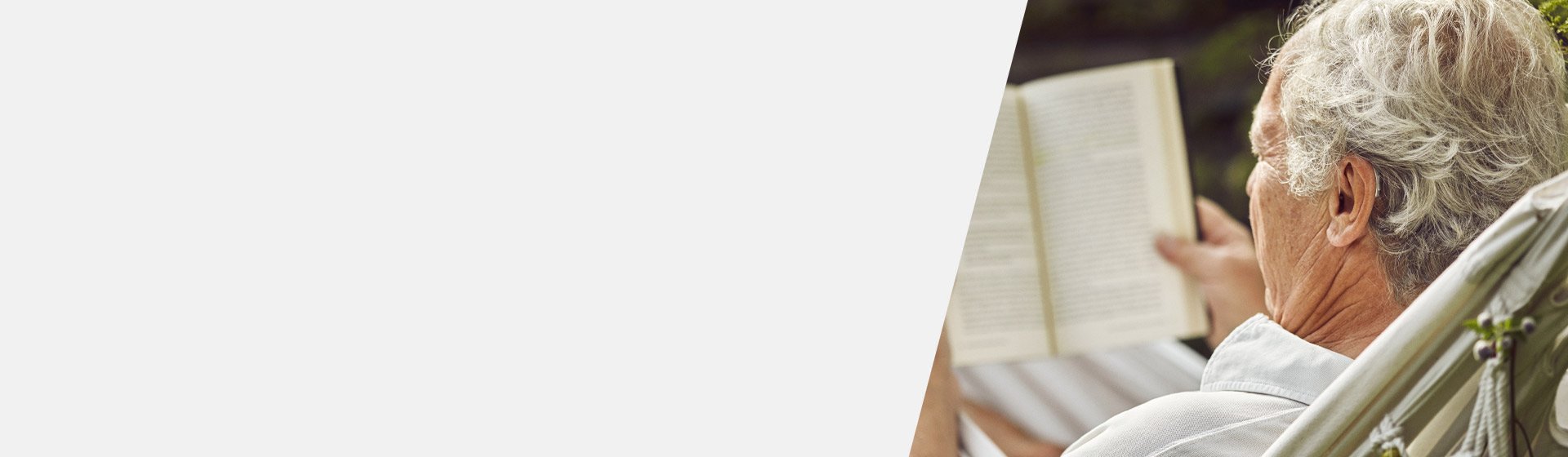 Senior man with a digital hearing aid relaxing outdoors and reading a book.