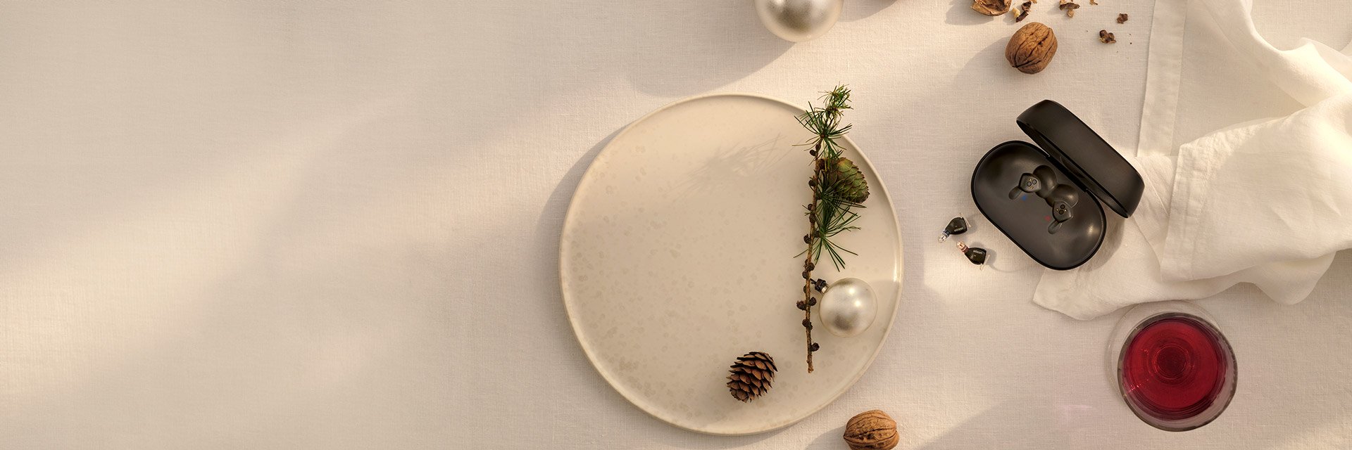 Oticon Zeal hearing aids displayed in a festive setting alongside a plate, holiday decorations, and a glass of wine to highlight their compact size.