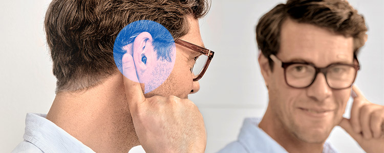A man touching his ear while wearing the Oticon Zeal hearing aid