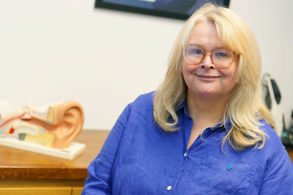 Hearing care specialist in a blue shirt sitting near a model of the human ear.