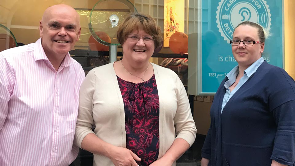 Hidden Hearing customer Christine Wright with two hearing care professionals outside a clinic.