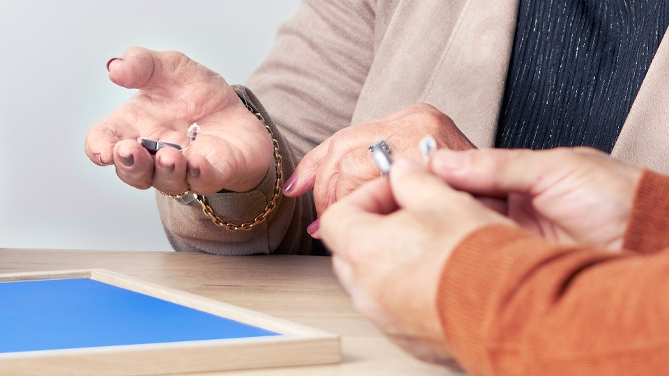 Two people discussing and holding hearing aids while seated at a table, highlighting hearing aid options and information.