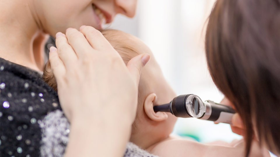 Baby receiving an ear examination with an otoscope while being held by a smiling adult