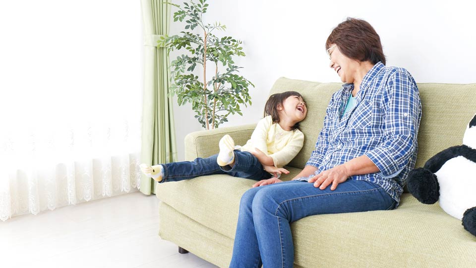 Grandmother sitting on a sofa smiling and interacting with her granddaughter in a bright living room.