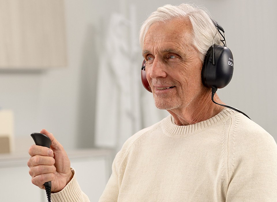 Man undergoing a professional hearing test using headphones and handheld device at Hidden Hearing.