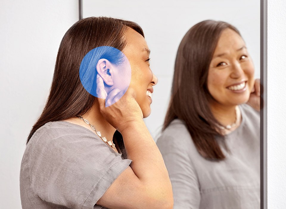 Oticon Zeal behind-the-ear hearing aid being adjusted by a woman in front of a mirror