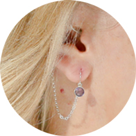 Decorative hearing aid jewelry with an amethyst gemstone and silver chain attachment.