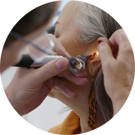 Image shows an audiologist using an otoscope to look inside a woman's ear