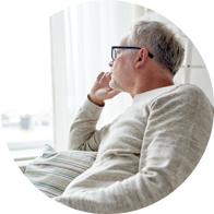 Man with short gray hair looking out of a window while sitting on a couch, appearing focused on an outdoor sound.