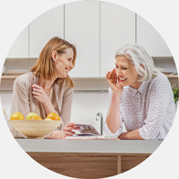 Mother leaning in to hear her daughter while sitting together in a kitchen.