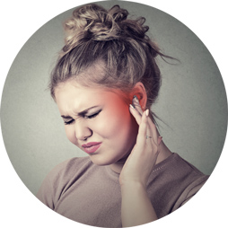 A person with their face obscured adjusts a discreet hearing aid behind their ear using their hand, set against a neutral gray background.