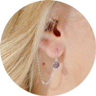 Decorative hearing aid jewelry with an amethyst gemstone and silver chain attachment.
