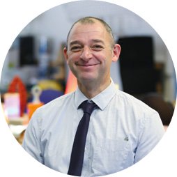 Hearing aid user Alex Slight wearing a formal shirt and tie in an office setting.