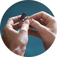 Close-up of hands cleaning and adjusting a hearing aid at Hidden Hearing.