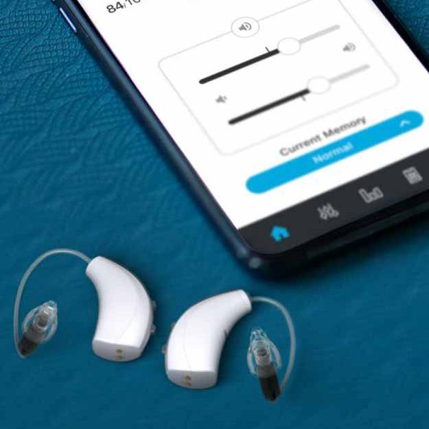 Starkey Livio hearing aids next to a smartphone displaying a hearing aid control app interface