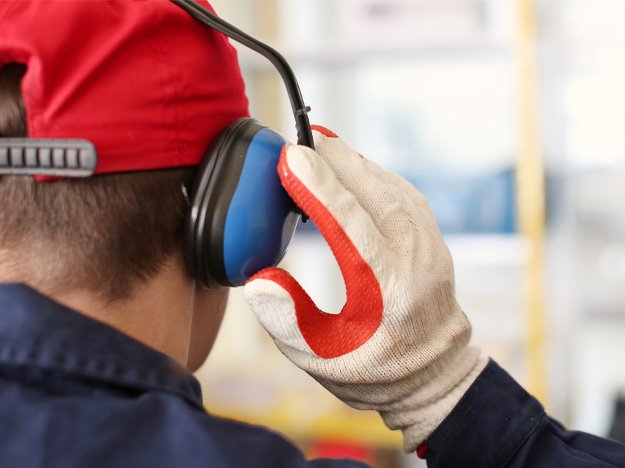 Man wearing protective earmuffs and gloves to shield ears from industrial noise.