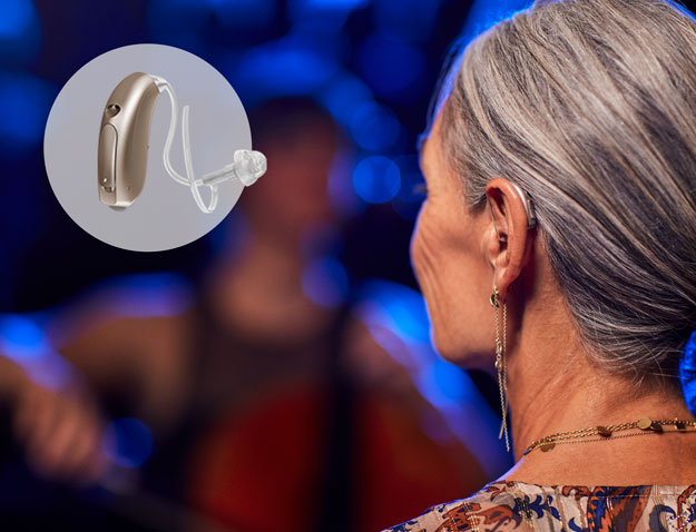 A woman with silver hair wears a discreet hearing aid from Oticon while attending a live music performance. A circular inset showcases the hearing aid's sleek design. Blue stage lighting enhances the ambiance.