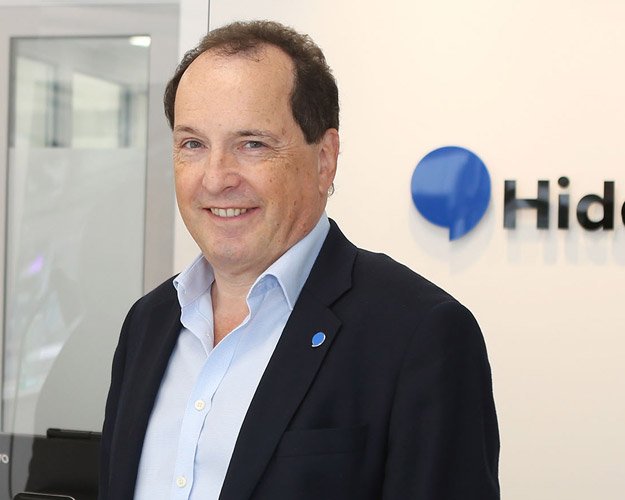 Hidden Hearing audiologist Timothy Humpidge standing in front of the company logo.