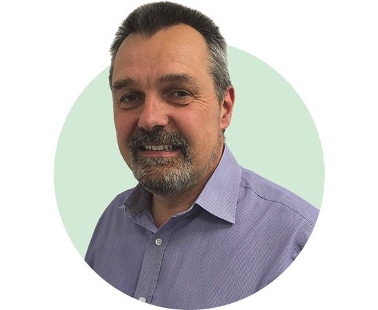 Hidden Hearing audiologist David in a light purple shirt against a green circular background
