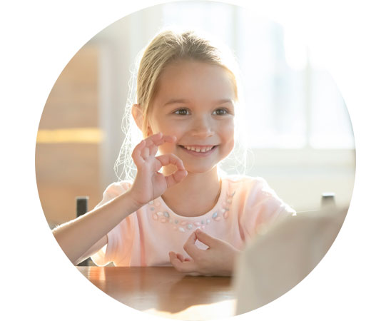 Child with hearing impairment using sign language in a brightly lit room.