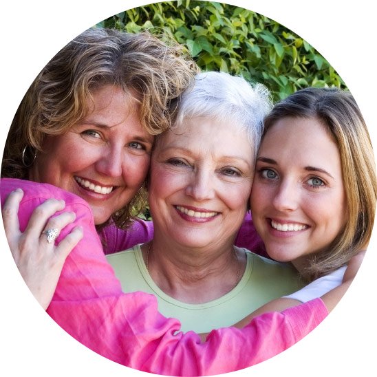 Three generations of women embracing outdoors in front of greenery