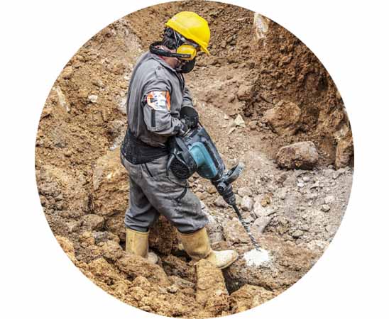 Builder wearing yellow hearing protectors and a hard hat while using a power drill in a construction site to prevent hearing damage.
