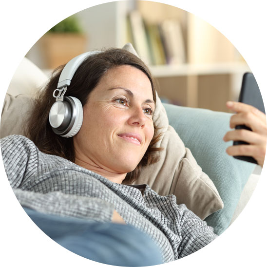 Woman wearing headphones and using a smartphone while lying on a couch.