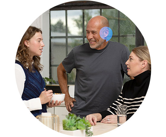 Conversation around a table highlighting hearing aid support in a social setting.