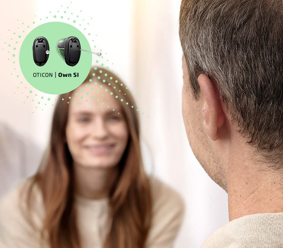 A man facing a seated woman in a hearing clinic discusses hearing care. A circular graphic showcases ’Oticon Own Si’ hearing aids, emphasizing advanced hearing aid technology for personalized hearing solutions.