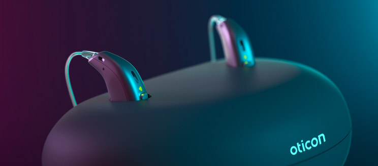 Rechargeable hearing aids on a charging dock with visible Oticon branding.