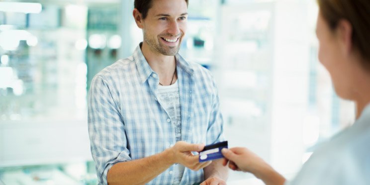 Man in a plaid shirt handing a credit card to a salesperson in a bright, modern store.